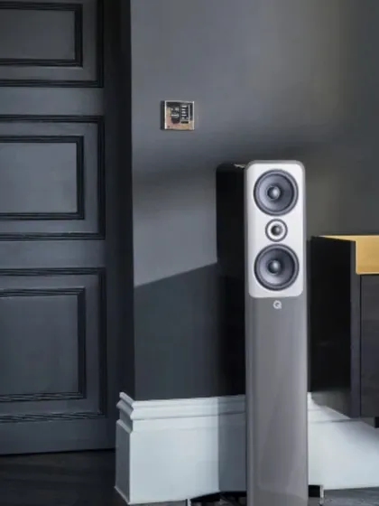 A closer look at the Q Acoustics floor-standing speaker in a sophisticated grey finish, placed next to a modern black door. This image highlights how slim tower speakers can fit elegantly into a room's corner without being obtrusive.