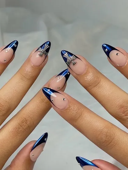 Edgy and glamorous, these almond nails showcase a deep blue metallic French tip on a natural base. Each nail is accented with delicate silver studs and a bold, cross-shaped chrome charm for a truly custom, high-fashion manicure.