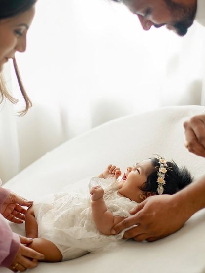 Parents looking down at their happy baby girl, who is lying on a soft cushion. A moment of pure, shared adoration.