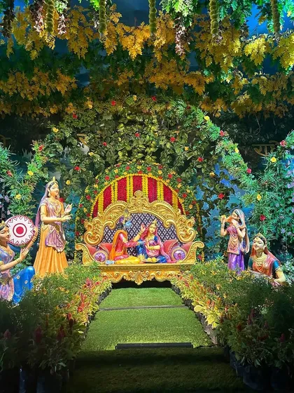 We recreated a scene from Vrindavan with this elaborate Janmashtami jhanki. The setup features lush greenery, a beautifully decorated throne for Radha and Krishna, and statues of gopis, making the story come to life.