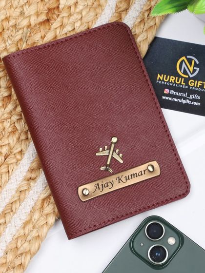 A maroon personalized passport cover with a simple name and airplane charm.