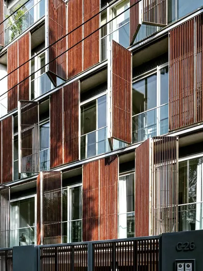 A multi-story residential facade featuring operable wooden screens. This allows residents to customize their environment, opening the screens for views and breezes or closing them for privacy and sun protection.