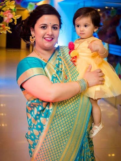 A mother in a beautiful turquoise saree holds her daughter, who is dressed in a sweet yellow dress. This portrait highlights the lovely traditional attire.