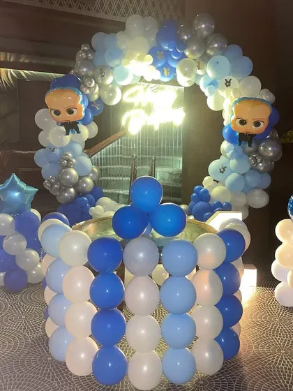 A 'Boss Baby' themed decoration for a first birthday party. The setup includes a balloon-wrapped cake table, a balloon arch, and Boss Baby character balloons, all in a classic blue and white color scheme.
