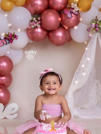 A happy birthday girl enjoying her pink cake, surrounded by a beautiful butterfly and balloon arch.
