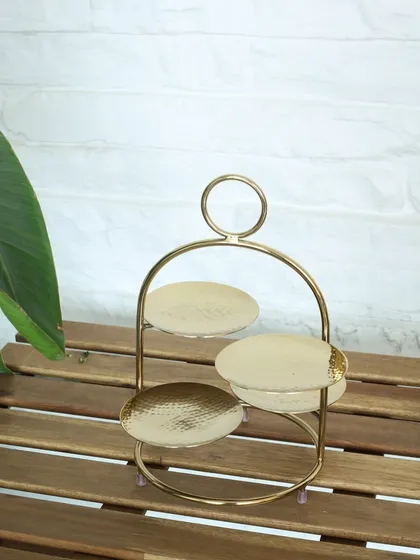 The Tête-à-tête stand, shown empty to highlight its elegant form. The three hammered gold plates are ready to be filled with your favorite treats for a stylish presentation.