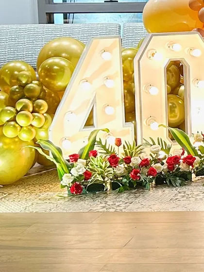 A close-up of a 40th birthday celebration, showing the large marquee '40' decorated with flowers and surrounded by gold balloons.