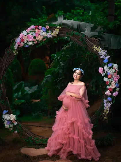 For a soft and romantic maternity look, I offer gowns like this beautiful pink ruffle dress. The gentle tiers of tulle create a dreamy silhouette, perfect for capturing the magic of this special time. This photo was taken at an outdoor location with a rustic floral arch.