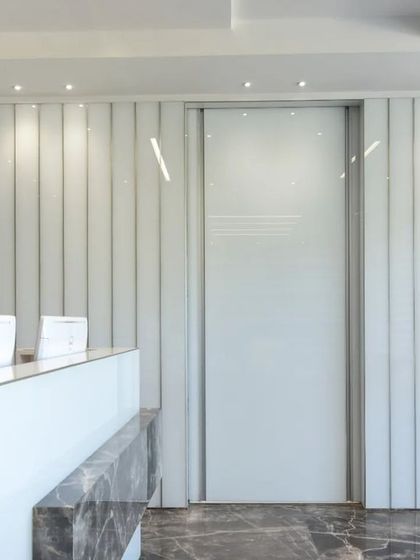 A sleek and modern workspace featuring a minimalist reception desk with a marble accent and a peek into a conference room with vibrant green chairs.
