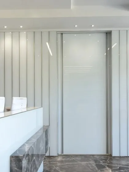 A sleek and modern workspace featuring a minimalist reception desk with a marble accent and a peek into a conference room with vibrant green chairs.