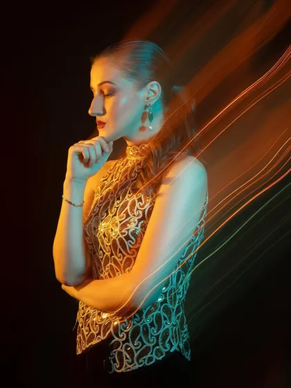 A thoughtful, profile pose. The light trails seem to emanate from the model, creating a magical effect.