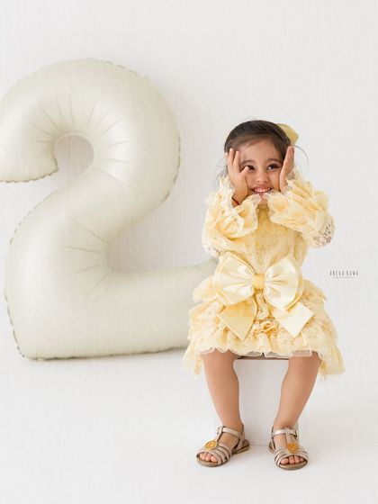 A playful and adorable portrait of a two-year-old girl. Her cute expression and the festive balloon make for a perfect birthday memory.