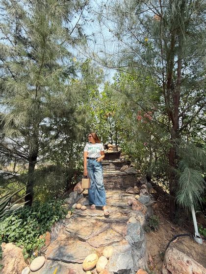 Travel and style energy. This casual look, featuring a graphic tee, bootcut jeans, and a straw bag, is perfect for a day of exploring in nature.