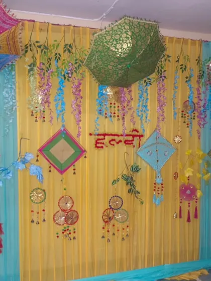 A colorful Haldi backdrop with yellow and light blue drapes. The decor features hanging umbrellas and various traditional ornaments for a fun and festive look.