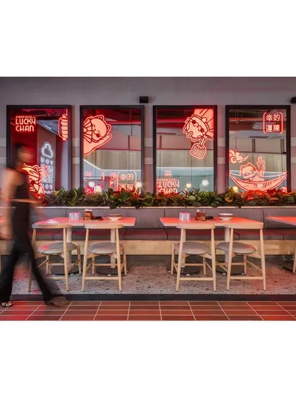 A person walking past the neon-lit windows adds a sense of movement and life to the space. The design is intended to be a dynamic backdrop for the activity of the restaurant.