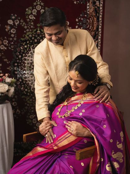 This image captures the loving bond between the couple, framed by the rich colors of her purple saree and the traditional decor of the studio setup.
