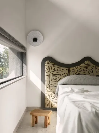 This bedroom in Pavilion House features a custom-designed headboard with a unique, graphic pattern. The window is strategically placed to frame a view of the landscape while maintaining privacy, embodying the home's 'living inside out' concept.
