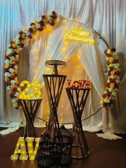 I combine classic and modern elements for a unique look. This anniversary setup features a circular frame decorated with a floral garland, a custom neon sign, and light-up marquee numbers for the anniversary year, all tied together with elegant draping.