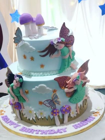 A magical two-tiered fairy cake. This design features delicate, handcrafted fairies with sparkling wings, surrounded by edible mushrooms and flowers in a whimsical garden setting.