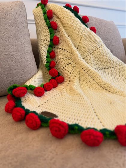 The cream-colored blanket with a red rose border, draped elegantly over a sofa. It shows how our blankets can instantly elevate your home decor.