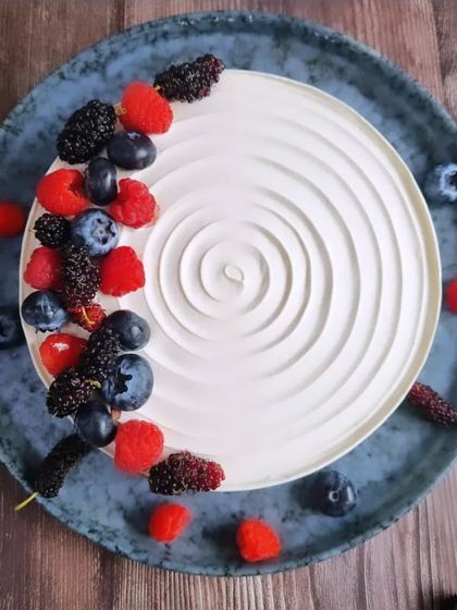 This beautiful mixed berry cake is topped with fresh blueberries, raspberries, and mulberries, arranged artfully over a swirl of white cream.