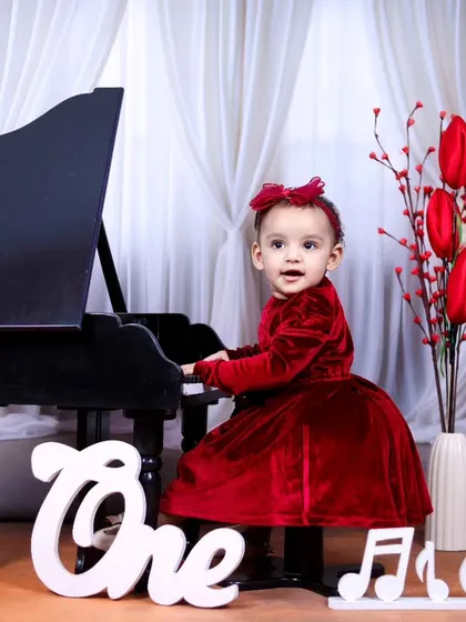 A one-year-old girl in a red velvet dress plays the piano in this elegant birthday setup.