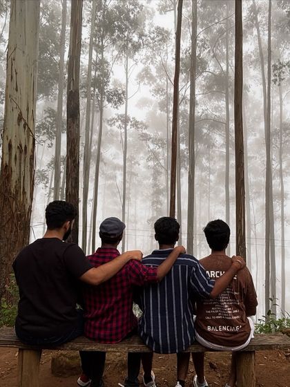 Friends sitting on a bench in the misty Kodaikanal forest.