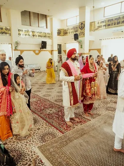 A wide shot of an Anand Karaj ceremony in a Gurudwara, capturing the couple and their families during the prayers.