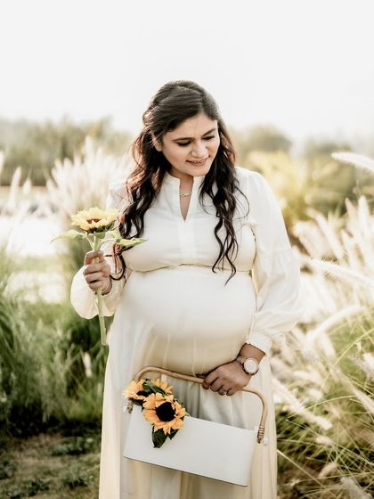 A serene portrait of the mom-to-be in a field of tall, soft grass, holding a single sunflower. Her gentle expression is full of peace.