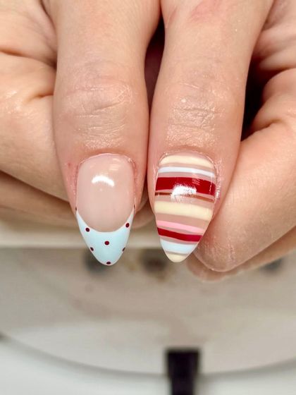 A playful and mismatched set featuring a modern twist on the French manicure. One nail has a baby blue tip with red polka dots, while the other features colorful stripes.