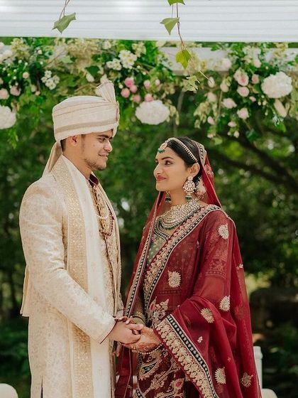 A couple shares a look of love, holding hands under a beautiful floral mandap.