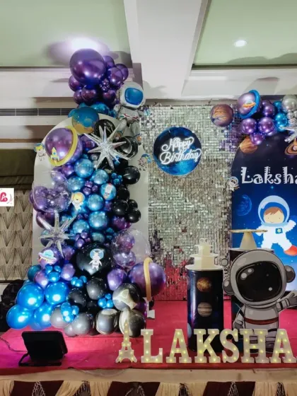 An out-of-this-world space theme for a 6th birthday party. This full stage decoration includes a silver sequin backdrop, a galaxy-themed balloon arrangement, an astronaut cutout, and large marquee lights for the name and age.