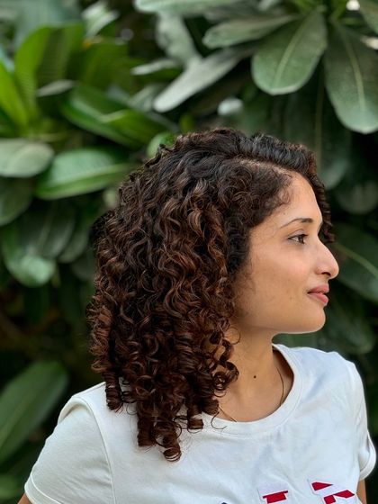 The side profile shows how the highlights are scattered throughout her hair to create a natural, sun-kissed effect on her curls.