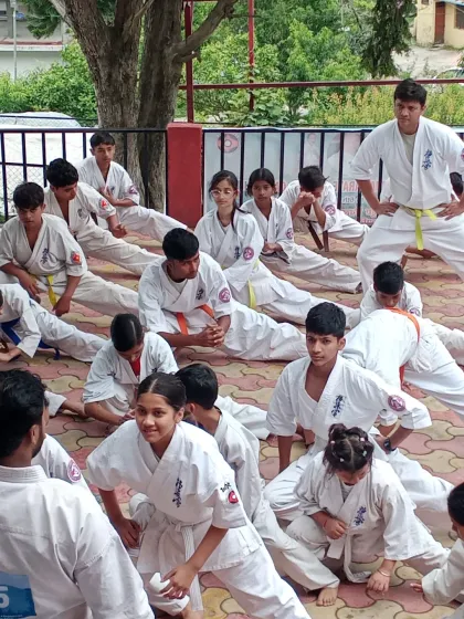 Students hold a deep stretching pose to improve their flexibility, which is crucial for high kicks and agile movements in karate.