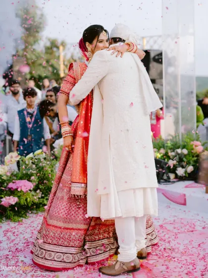 A shower of petals rains down as the couple shares their first hug as husband and wife at their hilltop wedding. A moment of pure, unadulterated happiness.