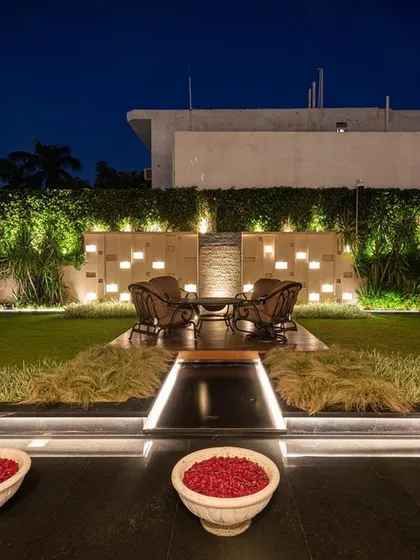 A beautifully lit seating area at the far end of a lawn, complete with a water feature and decorative bowls. The lighting design draws the eye through the space, creating an inviting destination for evening relaxation.