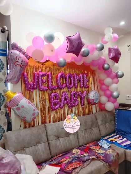 A 'Welcome Baby' girl setup with a pink shimmer curtain, a balloon arch, and various themed foil balloons.