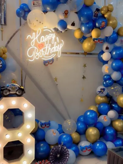 An 8th birthday party with a police car theme. The setup features a blue, gold, and white balloon ring, a light-up number '8', and a toy police car as a prop.