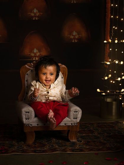 A happy baby boy sits in our traditional Diwali setup, his smile as bright as the festive lights.