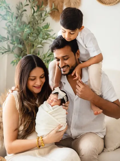 A playful and loving family portrait. The older brother gets a prime view from his dad's shoulders, all while the family adores their newest, tiniest member.