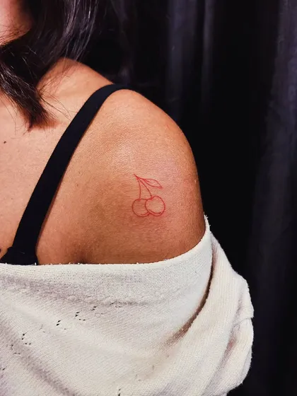 A playful cherry tattoo in red ink on the shoulder. This minimalist design adds a pop of color and a touch of fun.