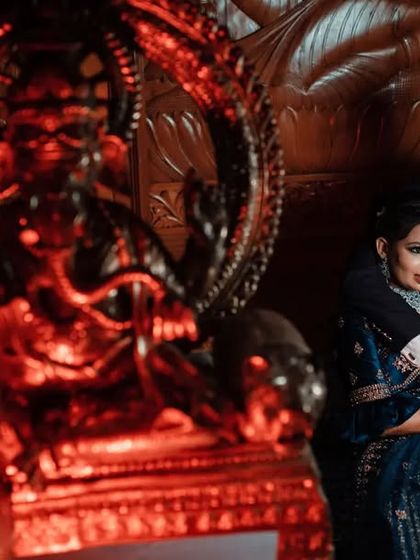 A dramatic and moody reception portrait. The red lighting on the Ganesha statue adds a powerful and artistic element to the photo.