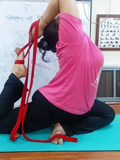 Another student practices Rajakapotasana with a belt, focusing on opening her chest and shoulders. The whiteboard in the background shows how we break down concepts like pranayama stages in our classes.