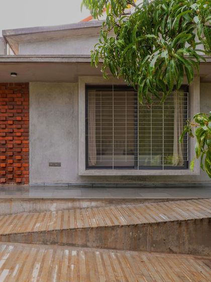 The east-facing service side of the house features a ramp for accessibility and an outdoor shower. The material composition of brick and raw cement stands out, creating a unique facade that is both functional and aesthetic.