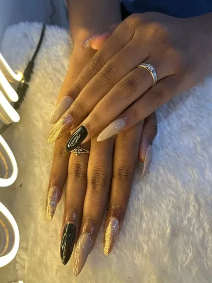 A full view of these dramatic stiletto birthday nails. The mix of nude, black, and gold glitter is so striking.