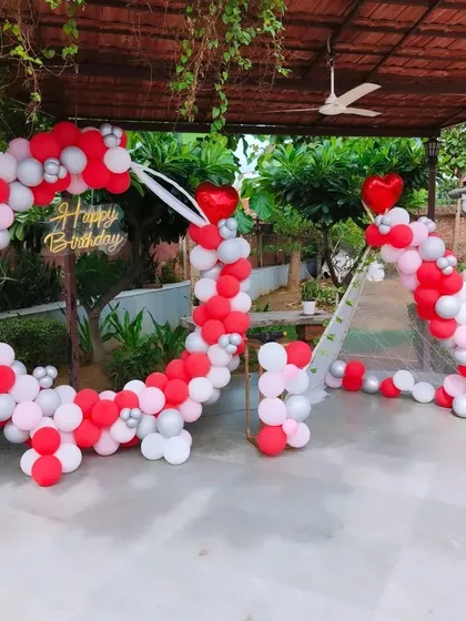 A heart-themed balloon decoration for an outdoor event. This large, heart-shaped arch is made of red, pink, and white balloons, creating a romantic and festive atmosphere.