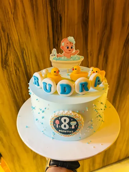 An 8-month milestone cake with a cute bathtime theme, featuring a baby in a tub and rubber duckies.