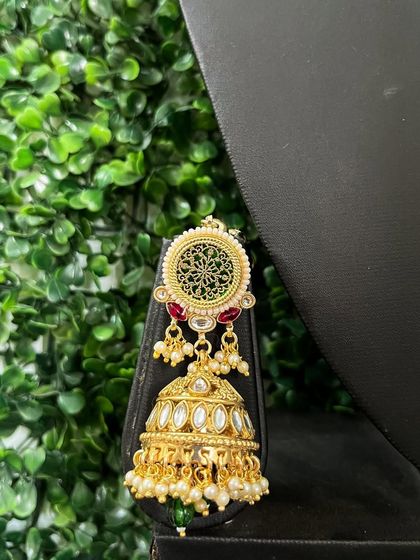 A close-up of a rental jhumka with intricate filigree work and red stone accents.