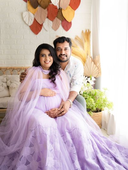 A sweet portrait of a couple looking directly at the camera, their hands joined over the baby bump.