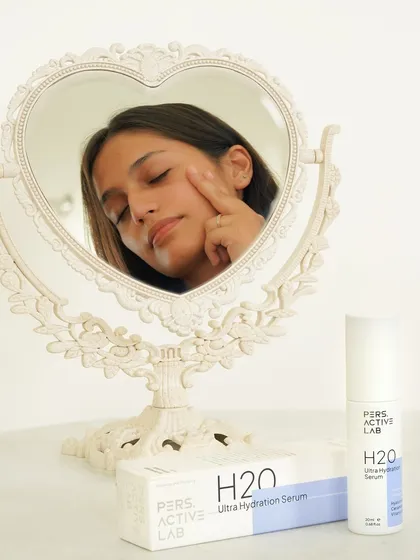 A clean, reflective shot showing a model applying serum, framed by a vintage-style mirror. This image combines a sense of classic beauty with modern skincare, highlighting the product's timeless appeal.